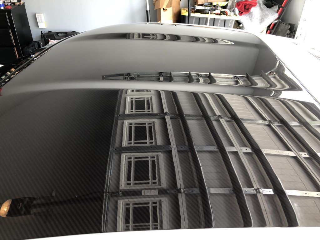 A car hood is reflected in a mirror in a garage.