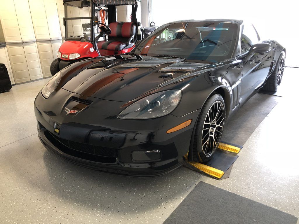 A black sports car is parked in a garage next to a golf cart.