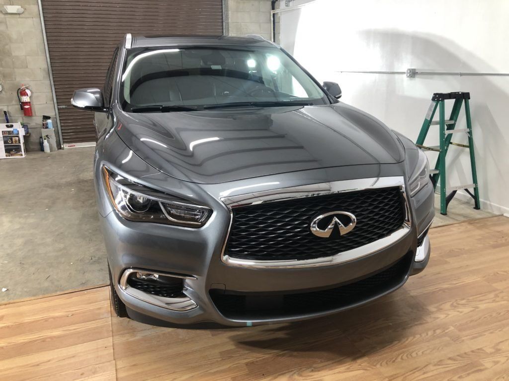 A gray infiniti q50 is parked in a garage next to a ladder.