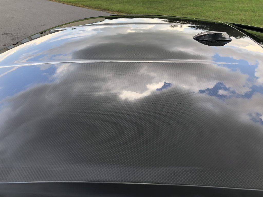 A close up of the hood of a black car with clouds reflected in it.