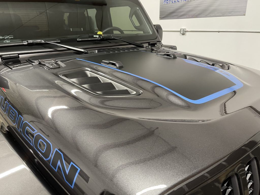 A black jeep with a blue stripe on the hood is parked in a garage.