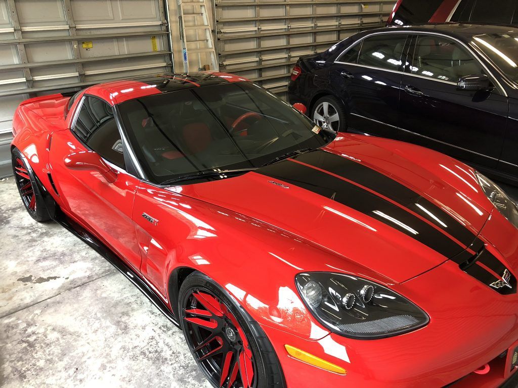 A red sports car is parked next to a black car in a garage.