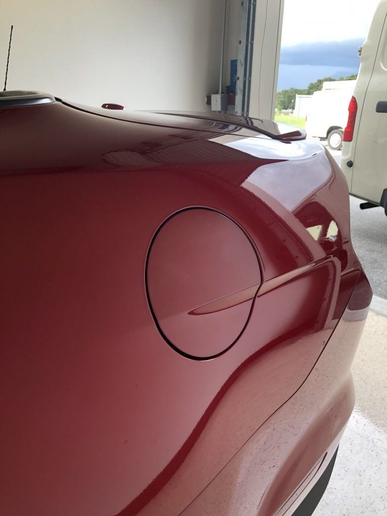A red car is parked in a garage with the hood open