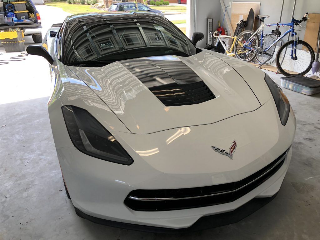 A white corvette is parked in a garage next to bicycles.