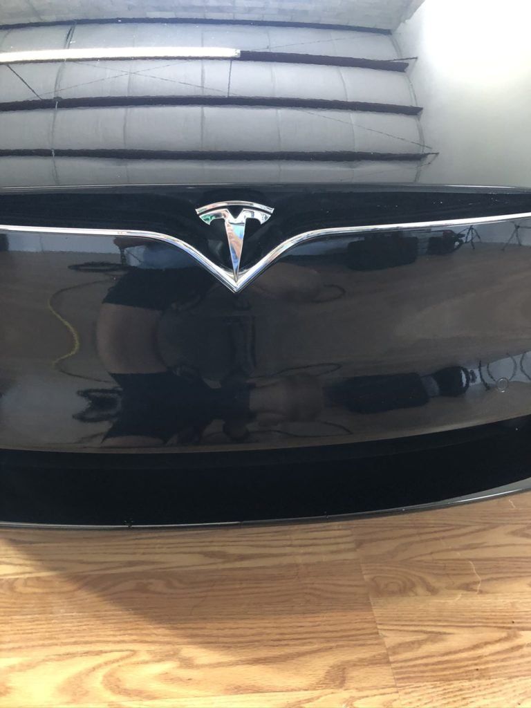 A black tesla model s is sitting on a wooden floor.