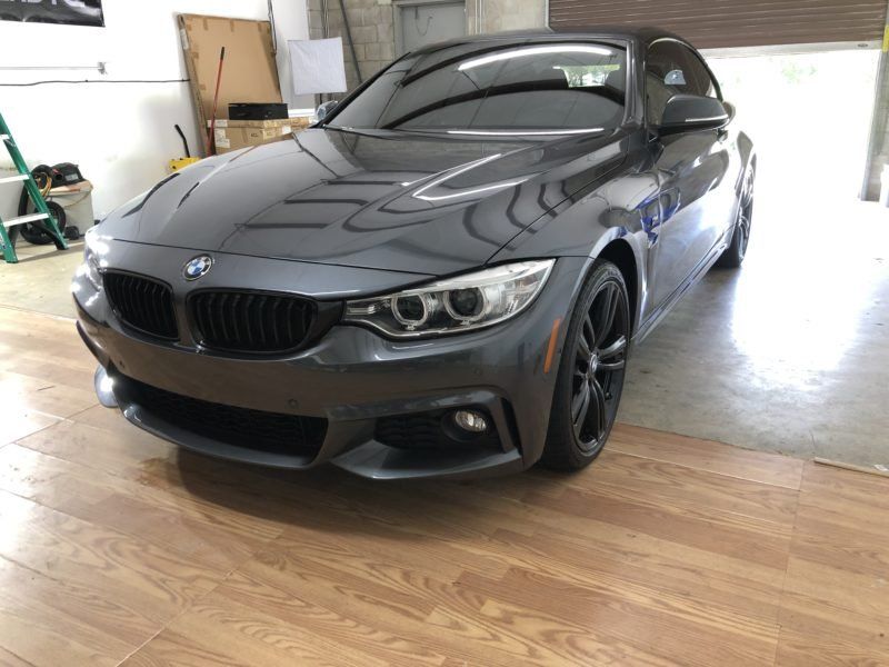 A gray bmw is parked in a garage on a wooden floor.