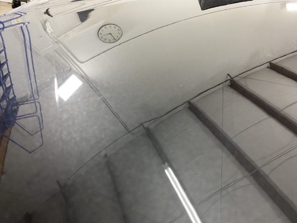 A close up of a car 's hood in a garage with a clock on the ceiling.