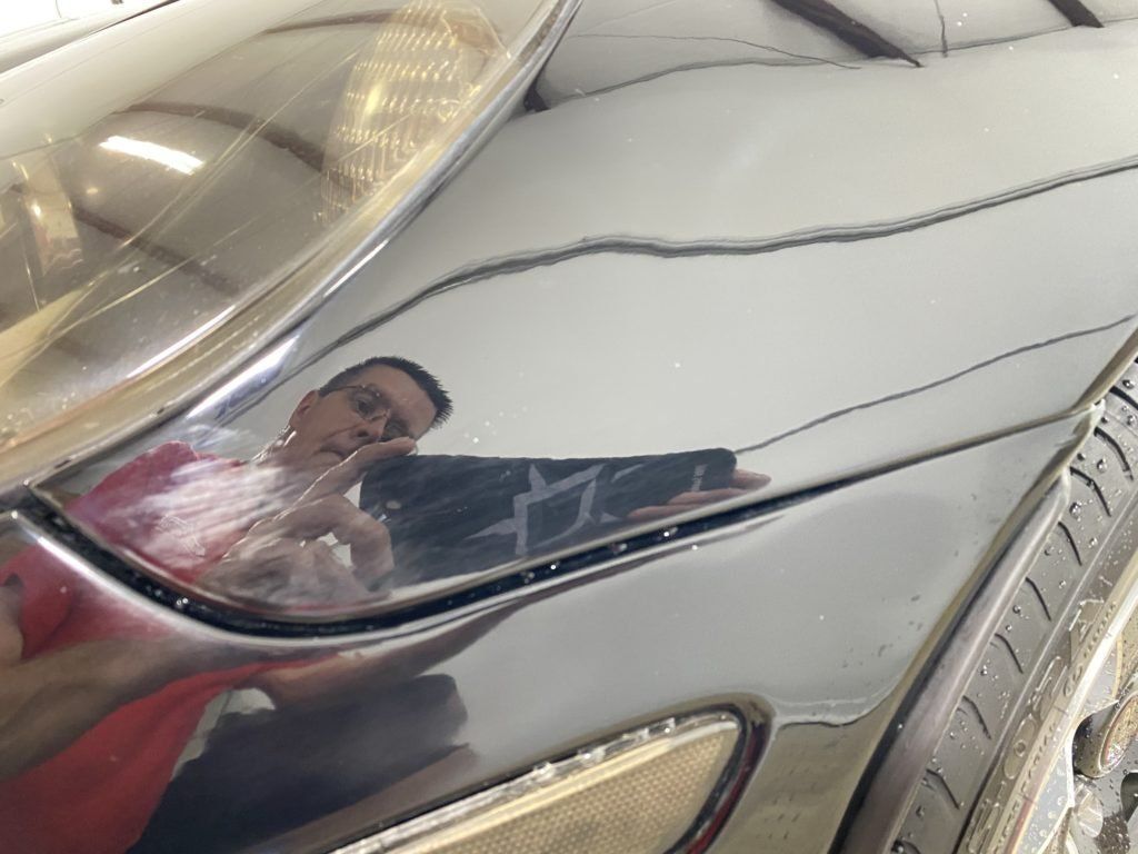 A man is reflected in the headlight of a car.
