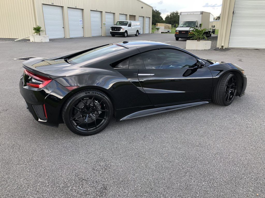 A black sports car is parked in a parking lot in front of a building.