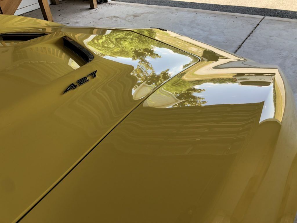 A yellow car is parked in a garage with the hood up