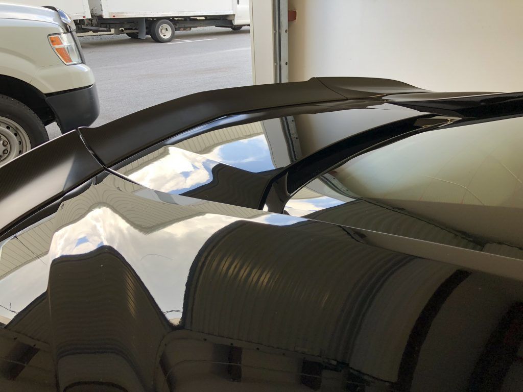 A black car is parked in a garage with a white truck in the background