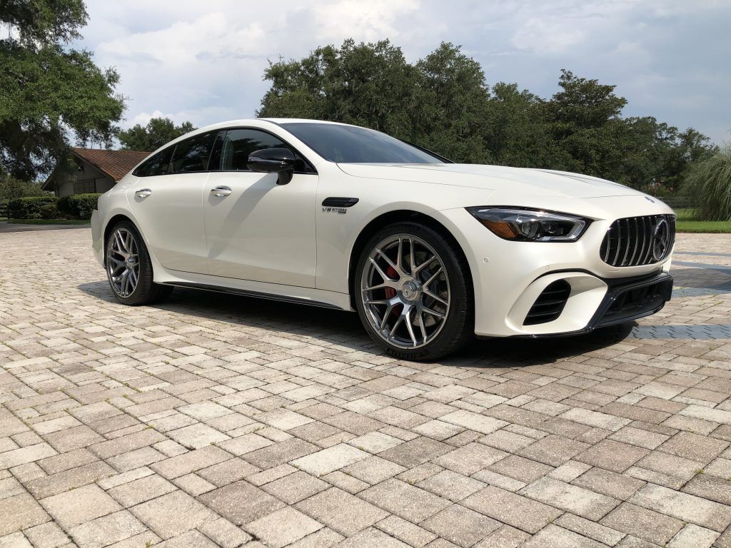 A white mercedes amg gt 63 s is parked on a brick driveway.