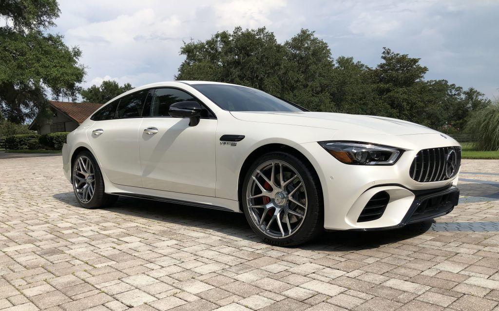 A white mercedes amg gt 63 s is parked on a brick driveway.