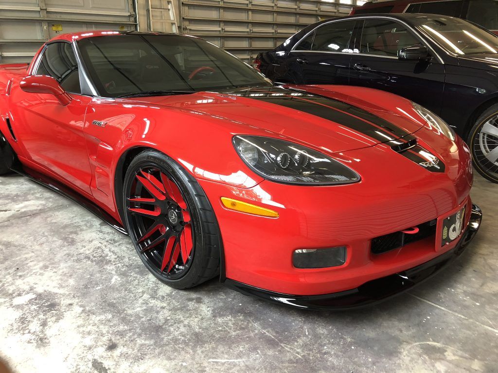 A red corvette is parked in a garage next to a black car.