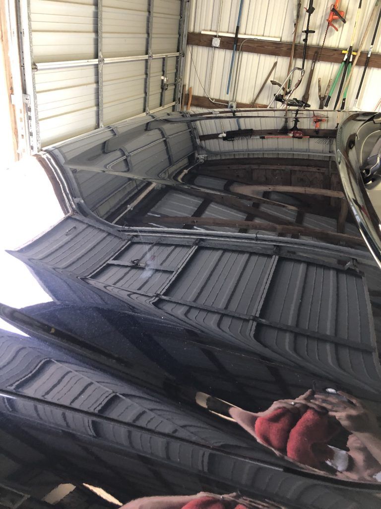 A black car is parked in a garage with the hood up.