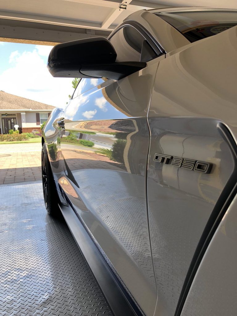 A silver mustang is parked in a garage next to a house.