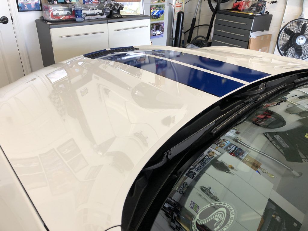 A white car with blue stripes on the hood is parked in a garage.