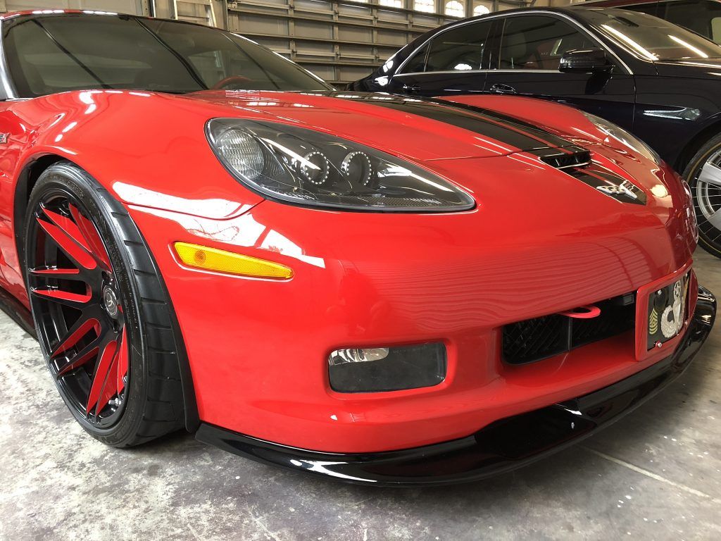 A red sports car is parked next to a black car in a garage.