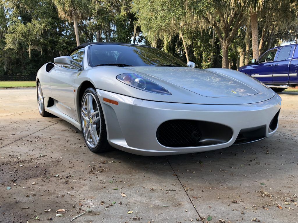 A silver sports car is parked in a driveway next to a blue truck.