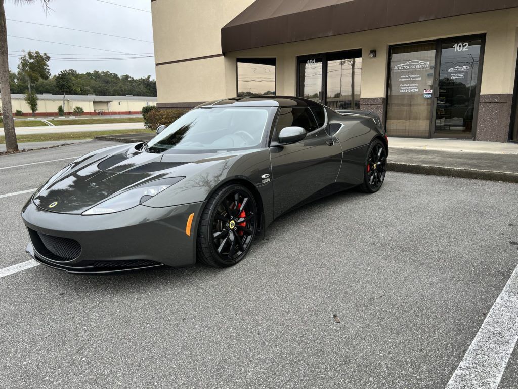 A gray sports car is parked in a parking lot in front of a building.
