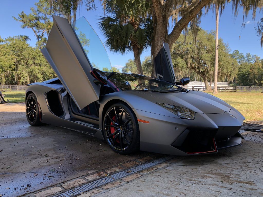 A lamborghini aventador is parked in a driveway with its doors open.