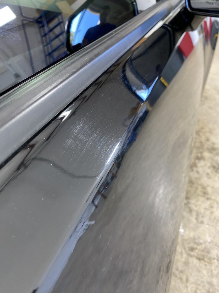 A close up of a car door with a reflection of a building in it.