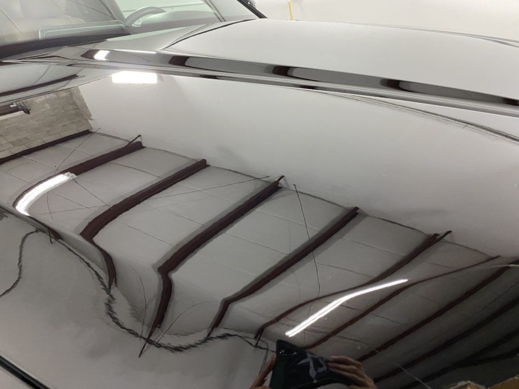 A person is taking a picture of a car 's hood in a garage.