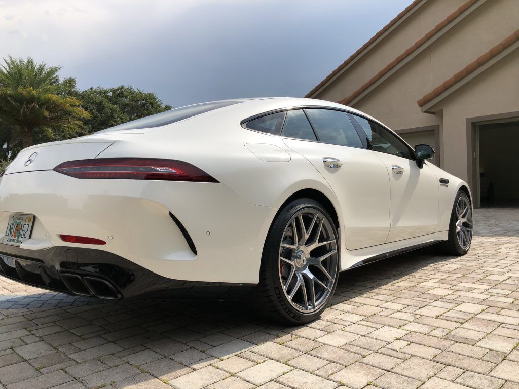 A white mercedes amg gt 63 s is parked in front of a house.
