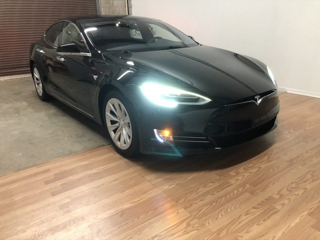 A black tesla model s is parked on a wooden floor in a garage.