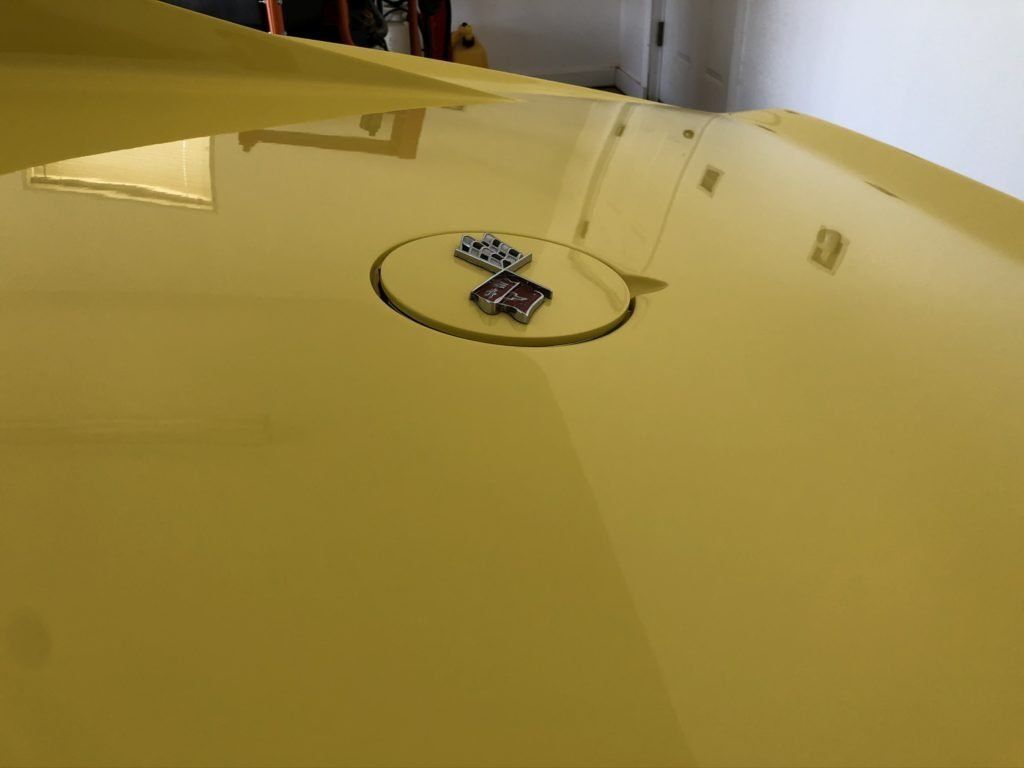A close up of a yellow car hood with a logo on it.