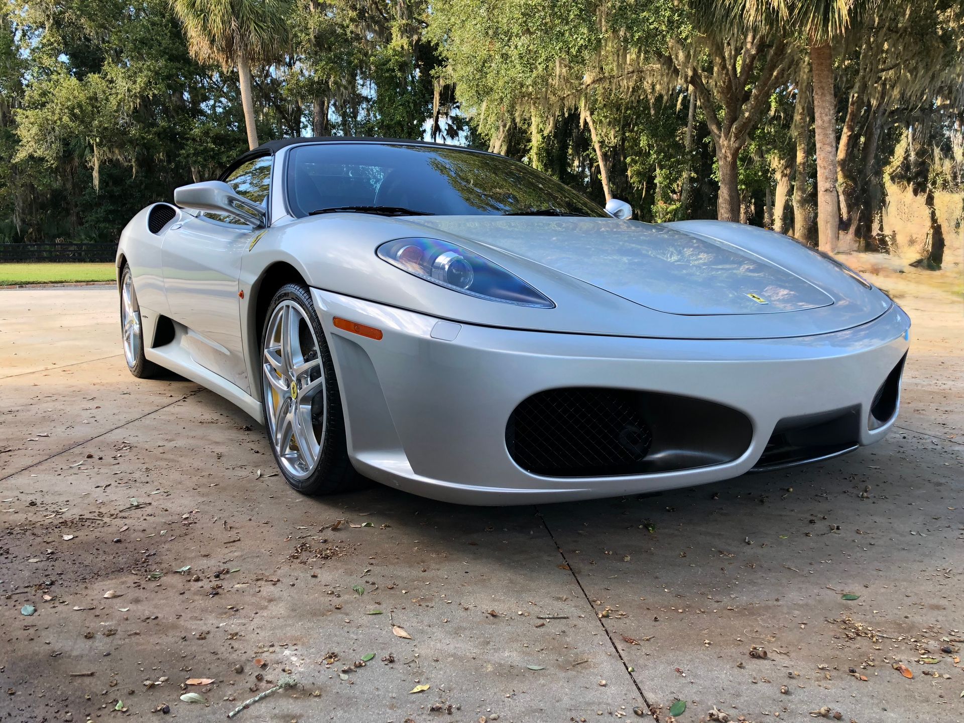 A silver sports car is parked in a driveway next to trees.