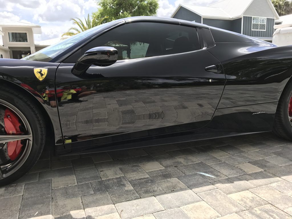 A black ferrari sports car is parked on a brick driveway.