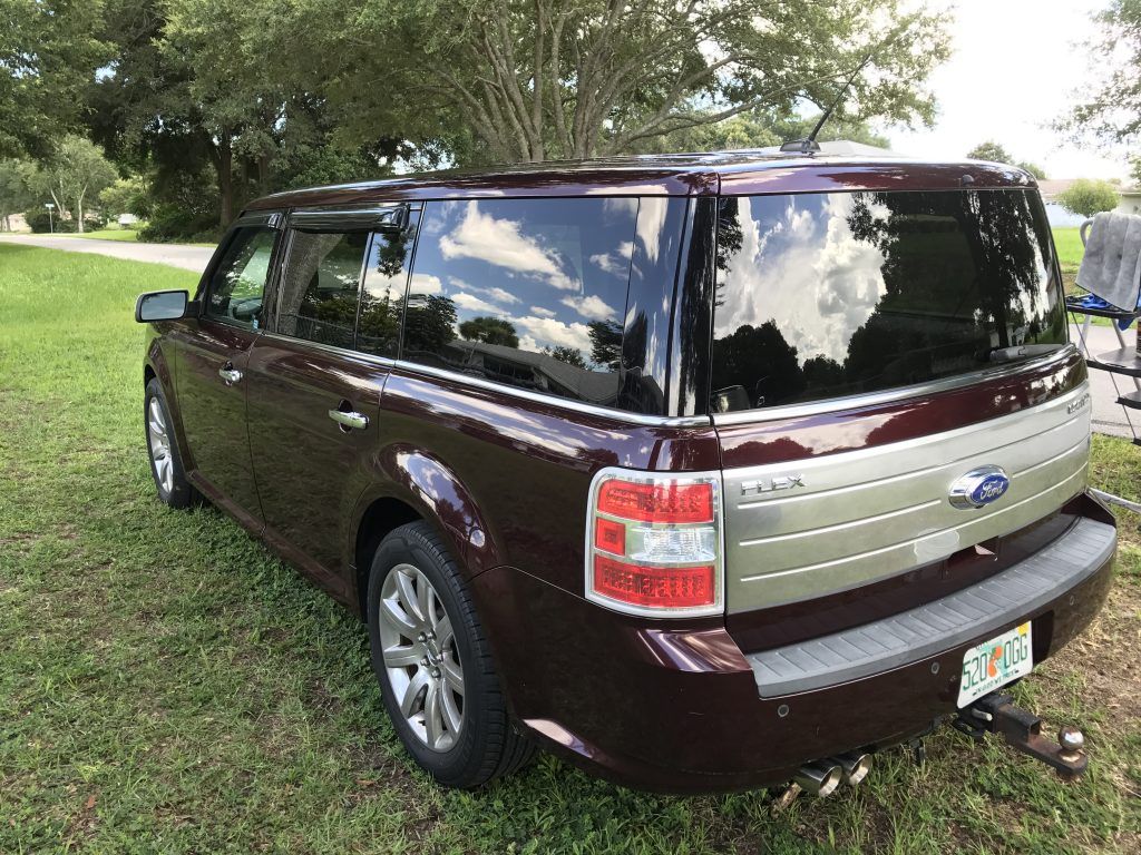 A brown ford flex is parked in a grassy field.