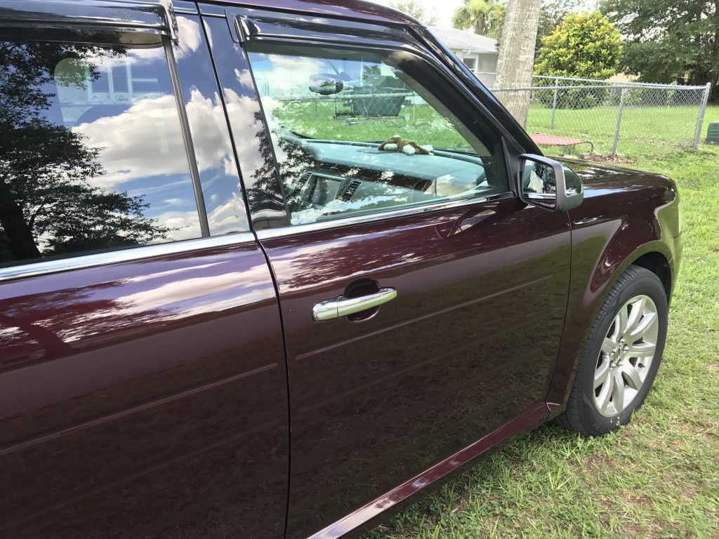 A burgundy ford flex is parked in a grassy field.