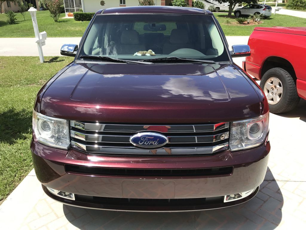 A red ford car is parked in a driveway next to a red truck.