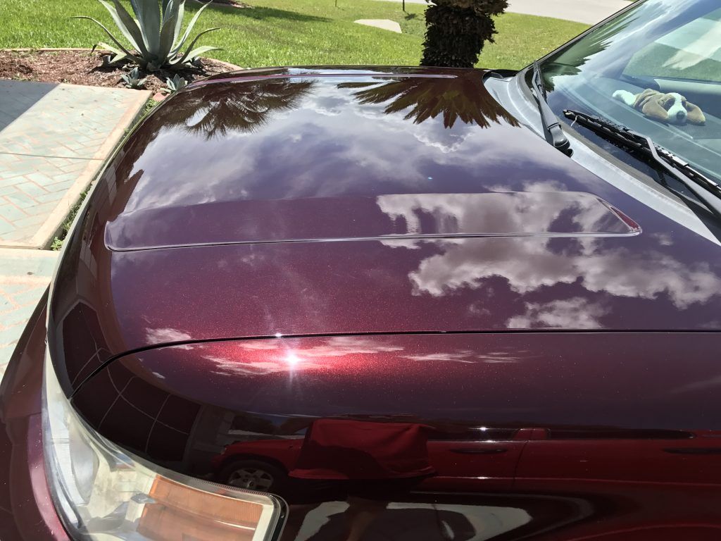 The hood of a red car is reflecting the sky and clouds.