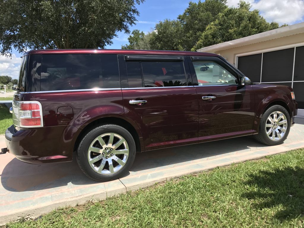 A red ford flex is parked on the side of the road in front of a house.