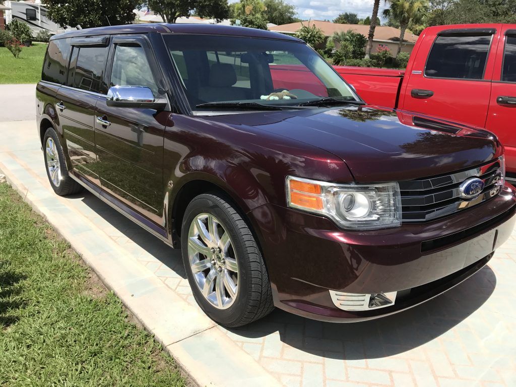 A burgundy ford flex is parked in a driveway next to a red truck.