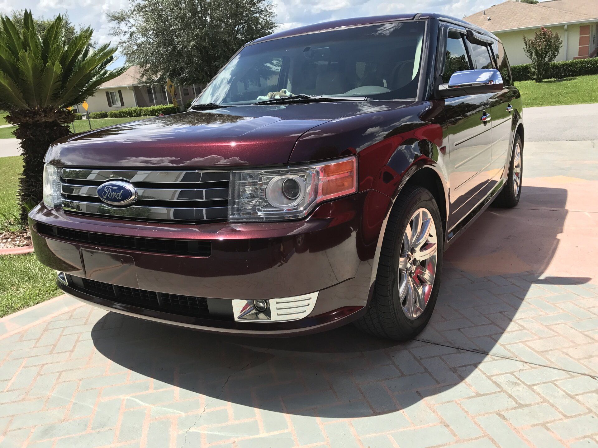 A red ford flex is parked in a driveway next to a palm tree.