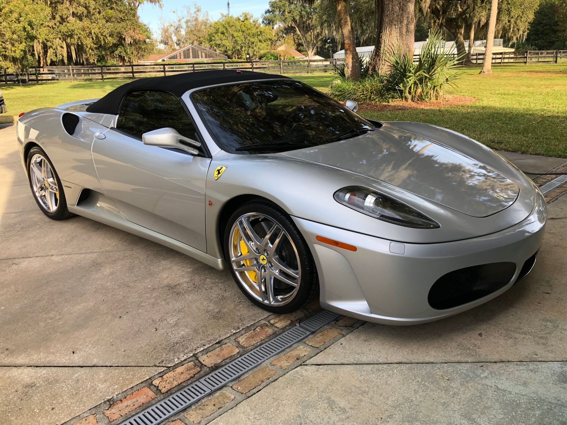 A silver ferrari convertible is parked in a driveway.
