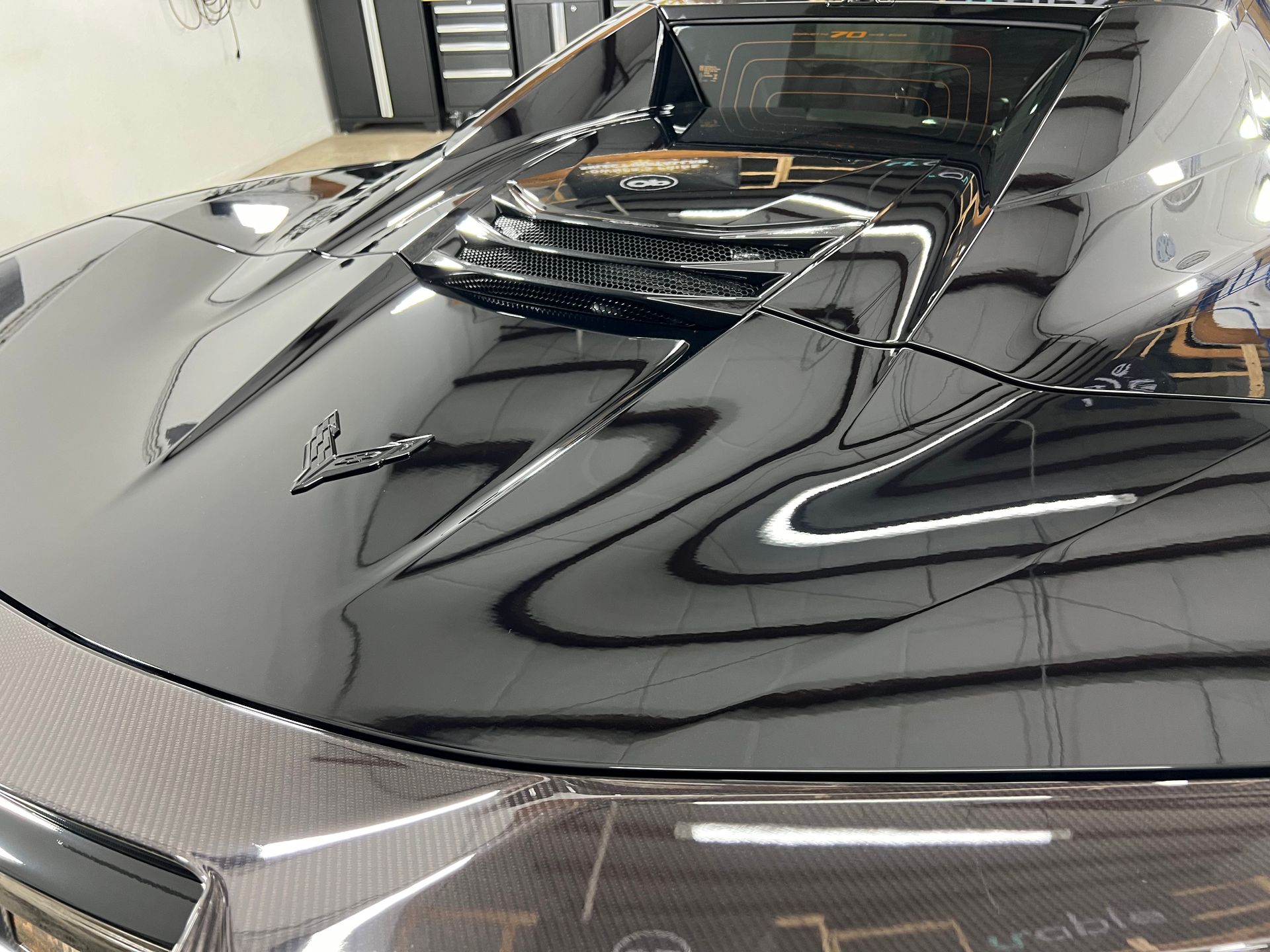 A black car is parked in a garage with the hood open.