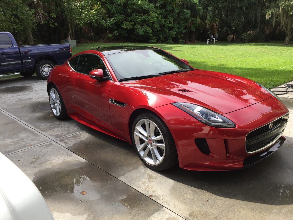 A red sports car is parked in a driveway next to a blue truck.