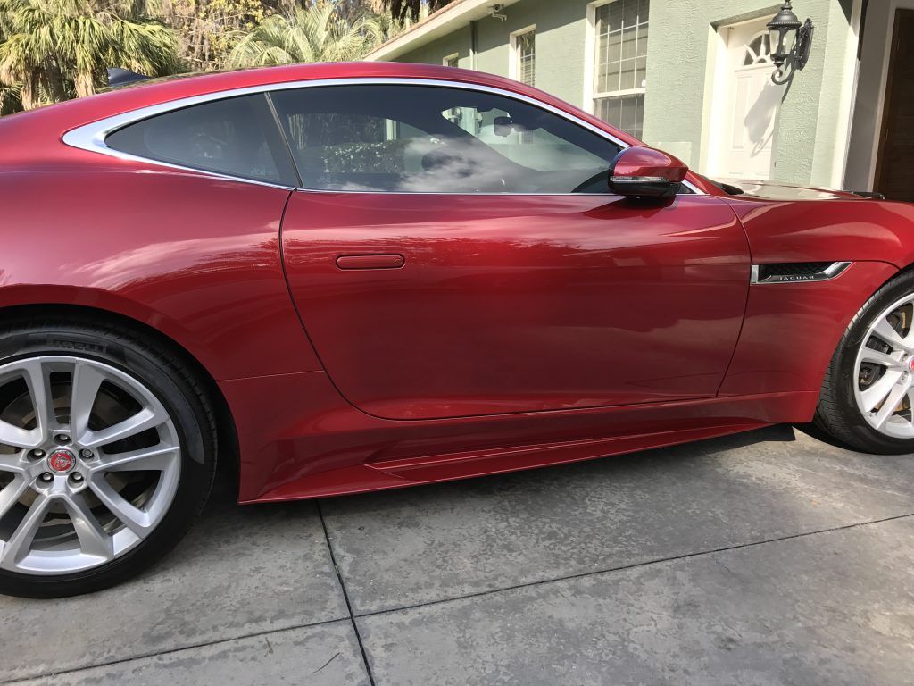 A red sports car is parked in a driveway in front of a house.