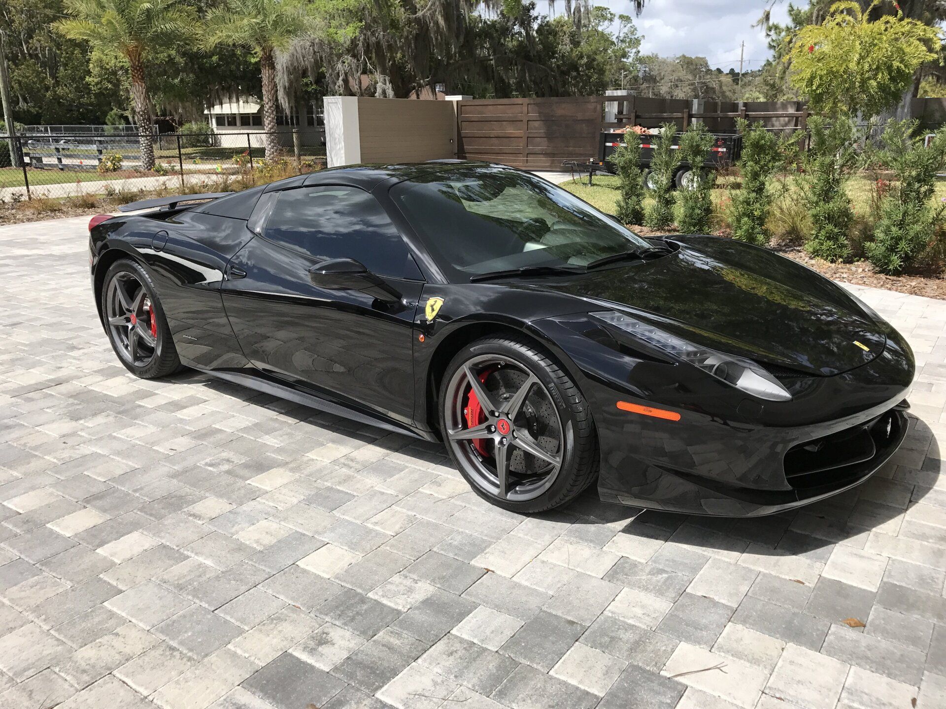 A black ferrari 488 spider is parked on a brick driveway.