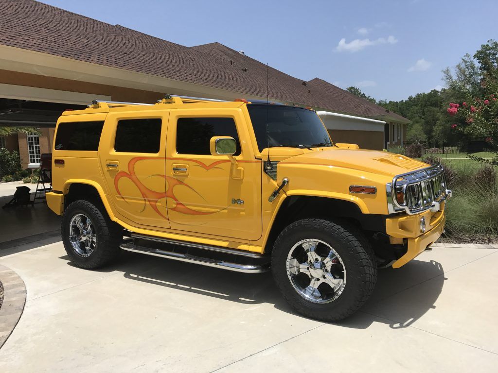 A yellow hummer is parked in a driveway in front of a house.