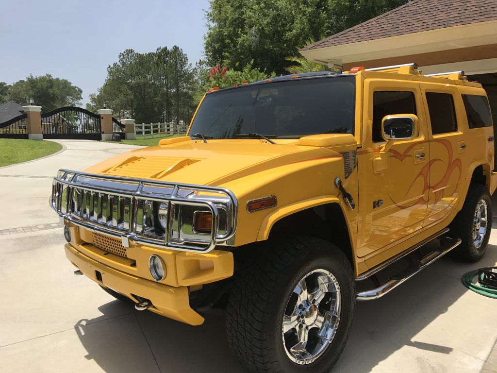 A yellow hummer is parked in a driveway in front of a house.