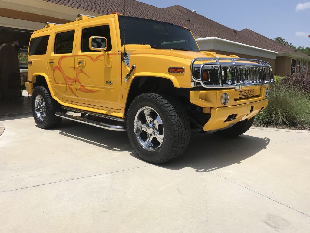 A yellow hummer is parked in a driveway in front of a house.