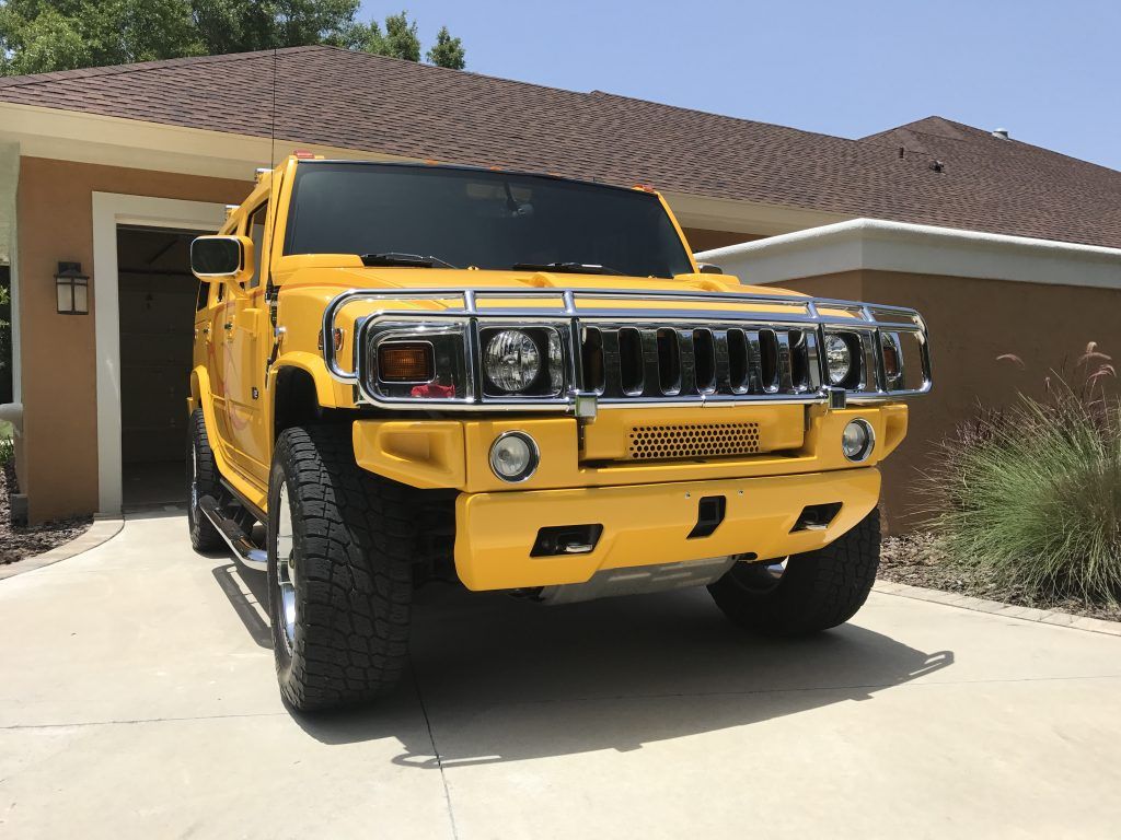 A yellow hummer is parked in front of a house.