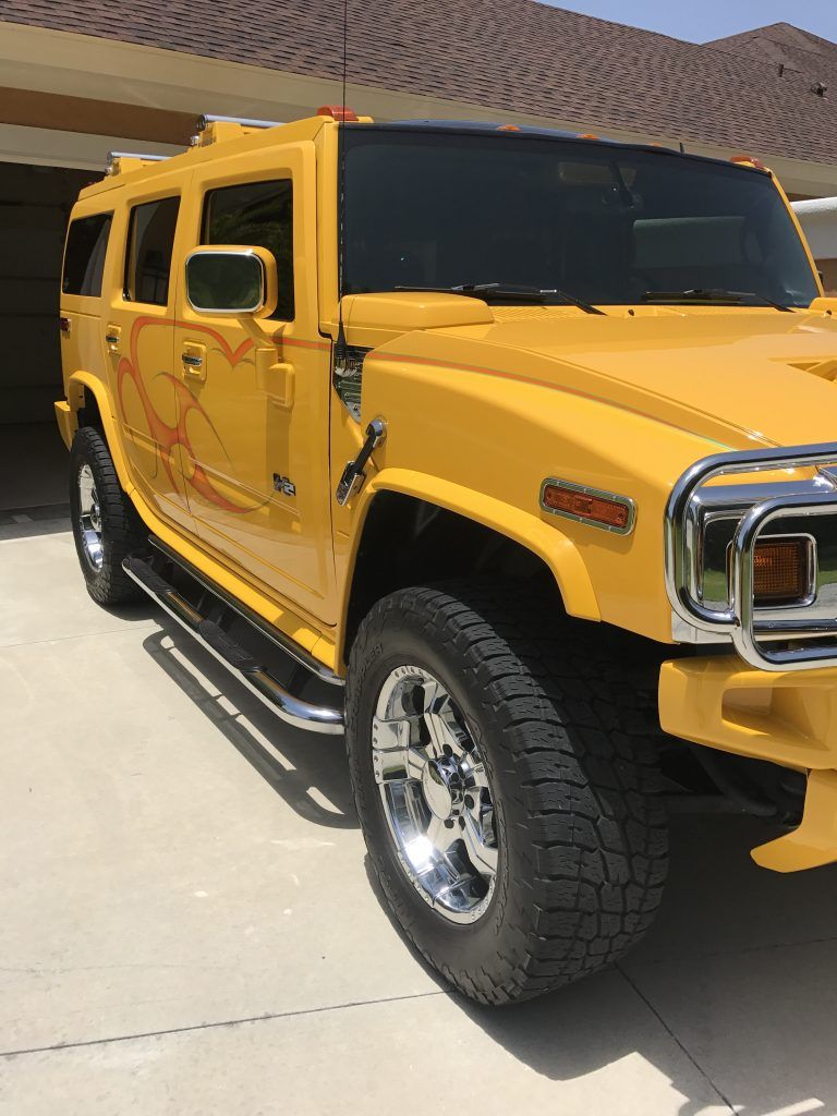 A yellow hummer is parked in a driveway in front of a house.