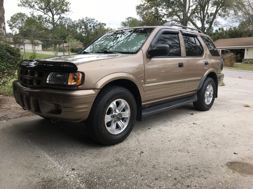 A brown suv is parked in a driveway in front of a house.